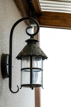 A black lamp is attached to the wall of the house from the outside. Vertical photo.