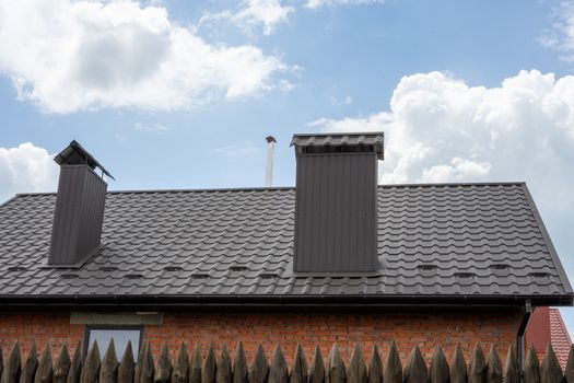 The upper part of the house is made of red brick. The roof of the house with a chimney. Blue sky and clouds