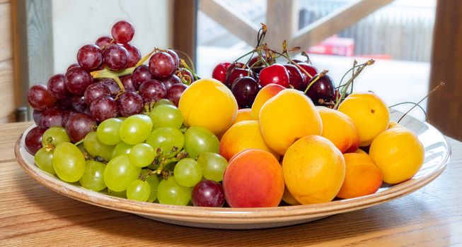 The Grapes of cherry and apricots lie on the plate. Ripe and Juicy Fruit