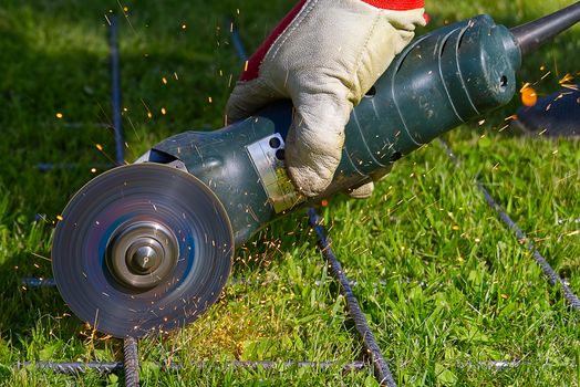 Cutting metal net with grinder on green grass. Sparks from contact materials. Worker outside, cut the steel net. Process with angle grinder