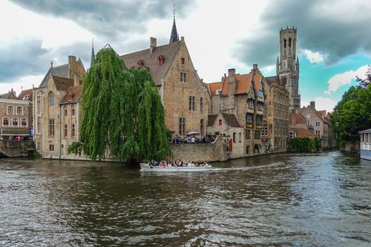 Bruges, Flanders, Belgium -  June 16, 2019: Shot of historic Brugge with Belfry and brown brick houses across canal. Most famous photograph spot at corner of Huidevettersplein.