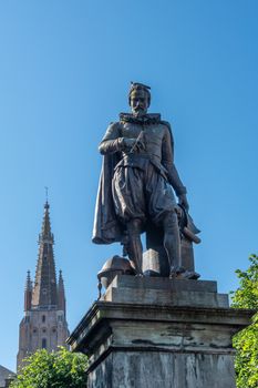 Bruges, Flanders, Belgium -  June 17, 2019: Simon Stevin statue with spire of OLV Cathedral in back under blue sky. Some green foliage. Pigeon on his head.