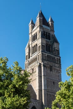 Bruges, Flanders, Belgium -  June 17, 2019: Brown brick stone tower of Sint Salvator Cathedral against full blue sky and with some green foliage.