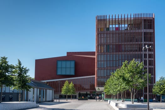 Bruges, Flanders, Belgium -  June 17, 2019: Contemporary red architecture of the Concert Hall or Concert Gebouw on the Zand square downtown. Blue sky, people and green foliage.