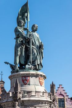 Bruges, Flanders, Belgium -  June 17, 2019: Closeup of Green bronze statue of Jan Breydel and Pieter De Coninck on Mark Square against full blue sky. Gables in back.