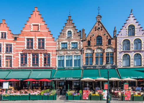 Bruges, Flanders, Belgium -  June 17, 2019: Brick stone facade row with step gables, now restaurants and bars with colored awnings, on NW side of Markt Square. Menus displayed.