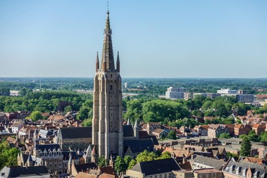 Bruges, Flanders, Belgium -  June 17, 2019: View South from top of Belfry tower, Halletoren, towards Onze-Lieve-Vrouw Church. Red roofs, lots of green foliage, railway station and flat country under blue sky.