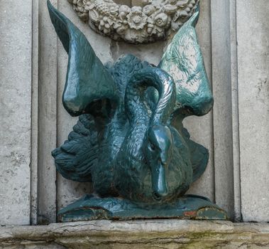 Bruges, Flanders, Belgium -  June 17, 2019: Closeup of green swan water pump set against gray stone. Neck and mouth is where water comes out.