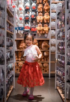 Cute little asian girl in dress with a doll in shop