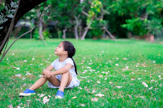 Cute asian little girl sitting in the park and looked up