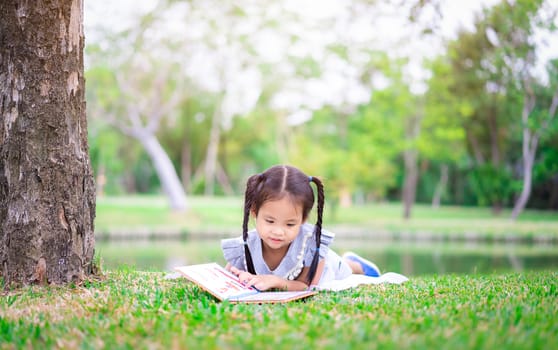 cute little girl  reading a book while lying in the park