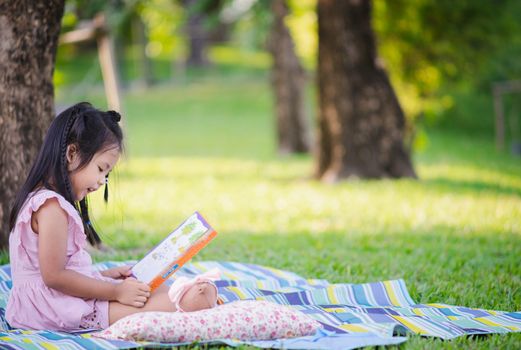 A little cute girl reading a book sitting under the tree