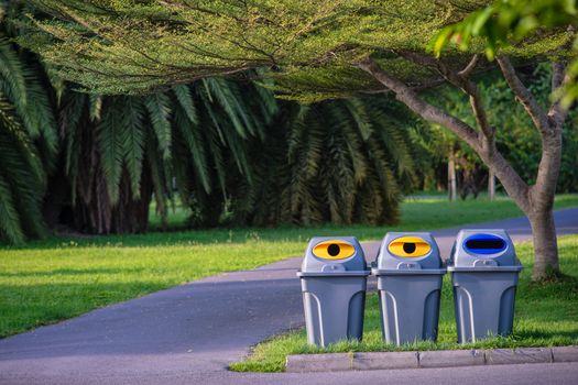 Three trashcans in a park with green tree and plants background in public park