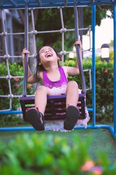 Asian little girl enjoys playing swing in a children playground