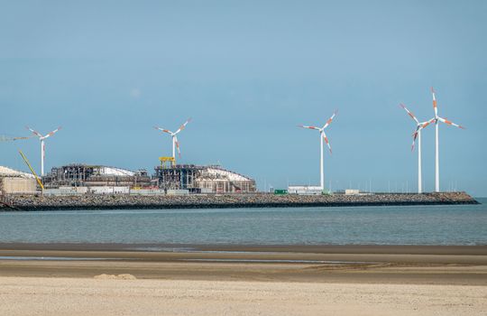 Zeebrugge, Flanders, Belgium -  June 18, 2019: Closeup of LNG terminal in port of Zeebrugge under blue sky as seen from beach in Knokke-Heist. Windmills on dock.