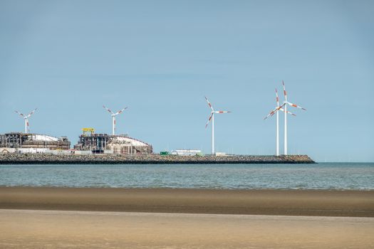 Zeebrugge, Flanders, Belgium -  June 18, 2019: Closeup of LNG terminal in port of Zeebrugge under blue sky as seen from beach in Knokke-Heist. Windmills on dock.