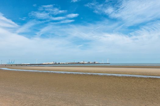 Zeebrugge, Flanders, Belgium -  June 18, 2019: Long shot on LNG terminal in port of Zeebrugge under blue sky with white stripes as seen from beach in Knokke-Heist. Windmills on dock.