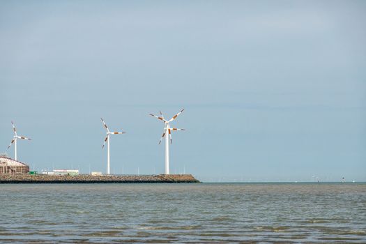 Knokke-Heist, Flanders, Belgium -  June 18, 2019: LNG terminal in port of Zeebrugge has windmils, but far on the horizon, barely visible, are more of them on Thorntonbank. Blue sky.