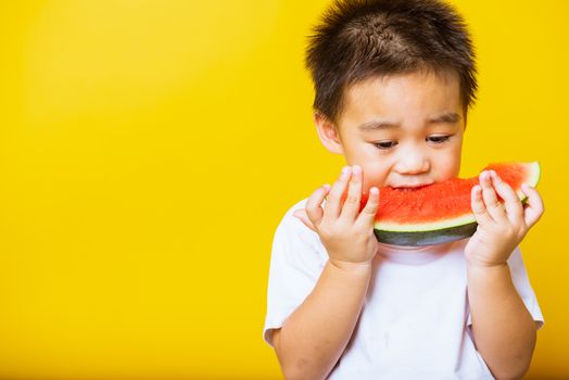 Happy portrait Asian child or kid cute little boy attractive laugh smile playing holds cut watermelon fresh for eating, studio shot isolated on yellow background, healthy food and summer concept