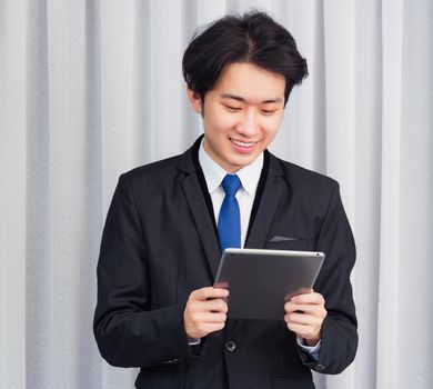 Work from home, Asian young businessman wear suit video conference call or facetime he smiling using smart digital tablet computer touching on screen at home office, looking to tablet
