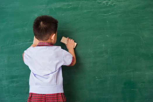 Back to School. Back of Asian cute little child boy kindergarten preschool in student uniform wiping clean or erase chalk on green school blackboard with sponge, First time to school education concept