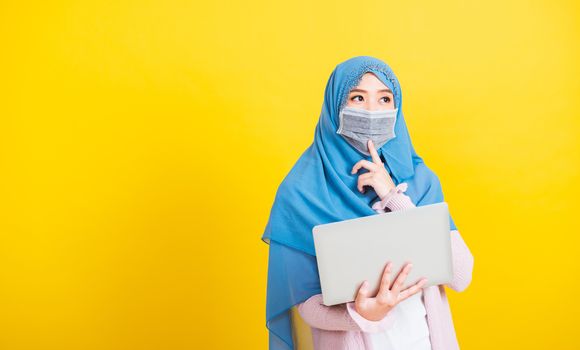 Asian Muslim Arab, Portrait of happy beautiful young woman Islam religious wear veil hijab and face mask protect she quarantines disease coronavirus hold laptop computer and thinking question