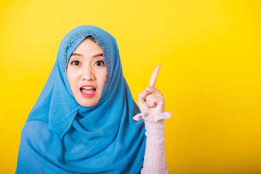 Asian Muslim Arab, Portrait of happy beautiful young woman Islam religious wear veil hijab funny smile she positive expression pointing with finger up to space isolated yellow background