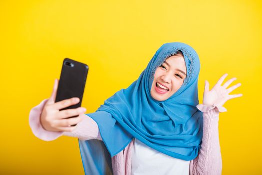Asian Muslim Arab, Portrait of happy beautiful young woman Islam religious wear veil hijab funny smile she taking making selfie with smart mobile phone, studio shot isolated on yellow background
