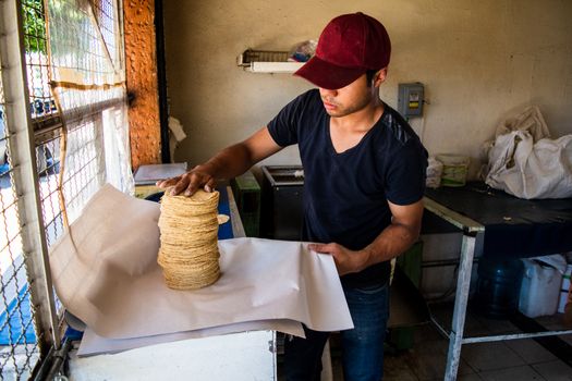 young man selling tortillas of nixtamal in typical mexican shop