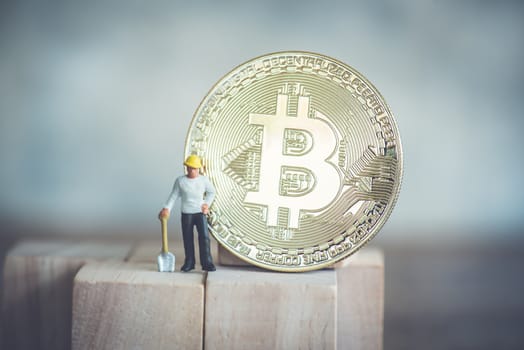 miniature worker with shovel stand on wood cube and gold bitcoin background