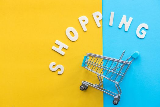 wood alphabet shopping and shopping cart on yellow and light blue paper background