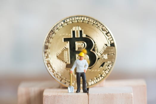 miniature worker with shovel stand on wood cube and gold bitcoin background