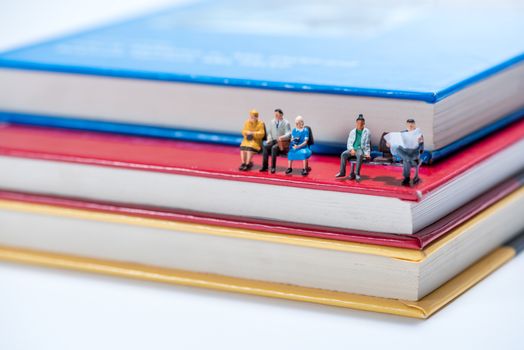 miniature people figure sitting on stack of book