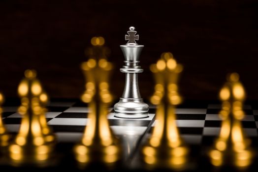 single silver king chess surrounded by a number of gold chess pieces , business strategy concept