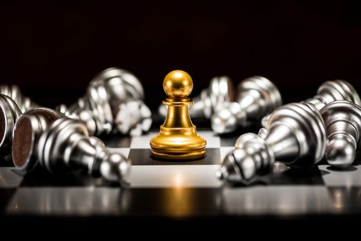 single gold pawn chess surrounded by a number of fallen silver chess pieces , business strategy concept