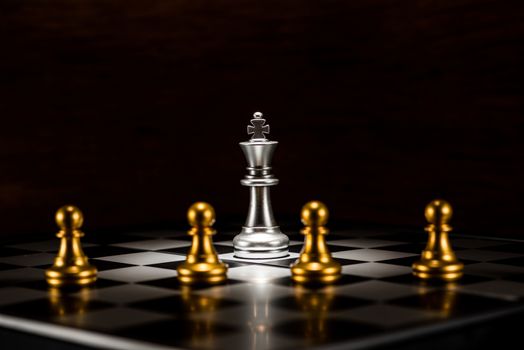 single silver king chess surrounded by a number of gold chess pawn pieces , business strategy concept