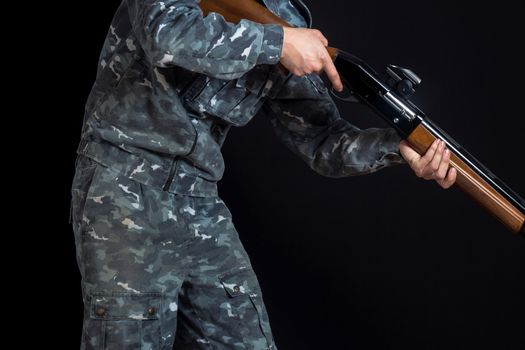 Military or hunter with a shotgun. A man holding a gun with a sight. Man in army uniform. Soldier, trooper on a black background. A man with a gun in camouflage military uniform.