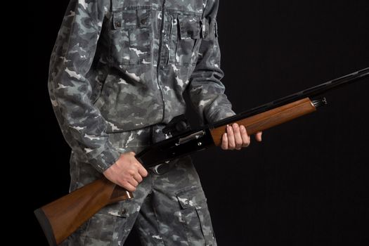 A man with a gun in camouflage military uniform. Military or hunter with a shotgun. Young man holding a gun with a sight. Man in army uniform. Soldier, trooper on a black background.