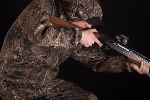 Hunter in camouflage clothing with a gun on a black background isolated. The man with the shotgun. Young guy in a camo suit with a gun. Soldier, trooper on a black background.