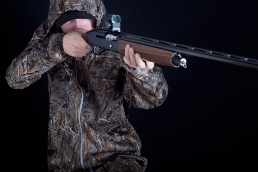 Hunter in camouflage clothing with a gun on a black background isolated. The man with the shotgun. Young guy in a camo suit with a gun. Soldier, trooper on a black background.