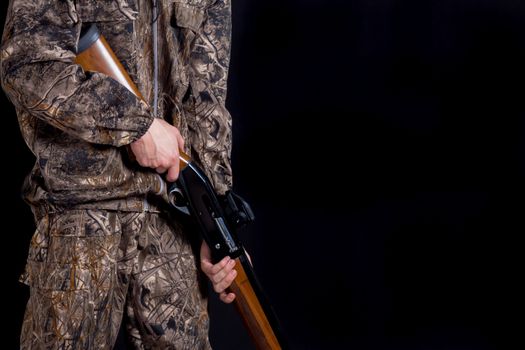 Preparation for spring or autumn hunting. Hunter in camouflage clothing with a gun on a black background isolated. The man with the shotgun. Young guy in a camo suit with a gun.