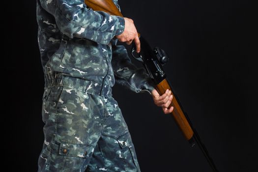 Young man with a gun. A soldier in military uniform with a shotgun. War games. Preparation for spring, autumn hunting. Soldier or hunter on a black background, isolated, copy space.