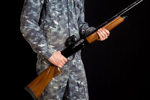 Soldier or hunter on a black background, isolated, copy space. Young man with a gun. A soldier in military uniform with a shotgun. War games. Preparation for spring, autumn hunting.