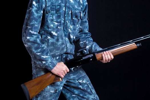 A soldier in military uniform with a shotgun. War games. Preparation for spring, autumn hunting. Soldier or hunter on a black background, isolated, copy space. Young man with a gun.