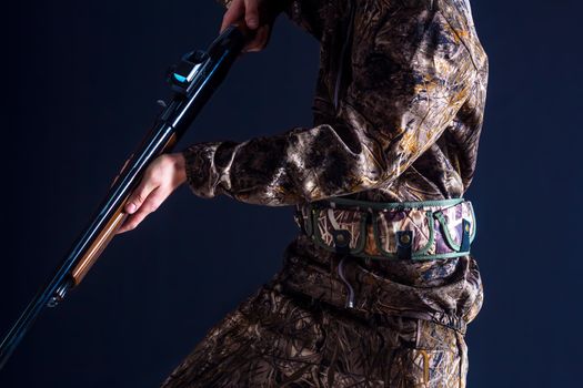 A military soldier of the US army in camouflage uniform with a weapon in his hands on a black background.Model of a hunter with a gun.Preparation for spring or autumn hunting.The man with the shotgun