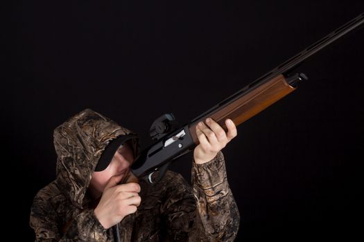 The man with the gun aims. Hunter in camouflage clothes with a shotgun on a black background. Military with weapons. Copy space. Preparation for spring or autumn hunting.