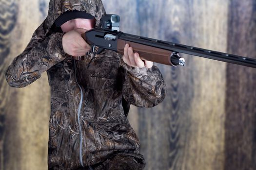 Hunter in camouflage clothing with a gun on wooden background. The man with the shotgun. Young guy in a camo suit with a gun. Soldier, trooper on on wooden background