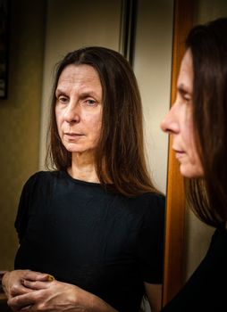 Portrait of an adult woman with long hair and crossed hands reflecting in a mirror in a dark room