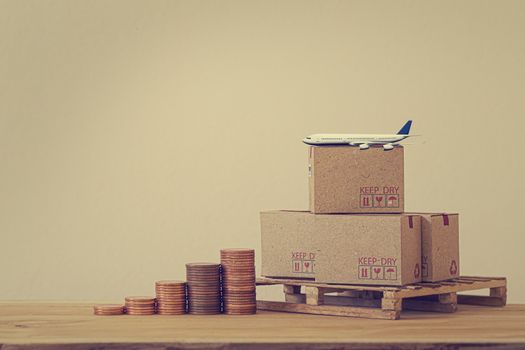 Modern business, online shopping concept : Arrange step coin and cardboard boxes for packing of goods with plane on wood pallet. Worldwide shipping service to increase channels Business and finance