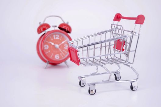 Shopping cart and classic alarm clock on white background. Sale time buy mall market shop consumer concept. Selective focus.